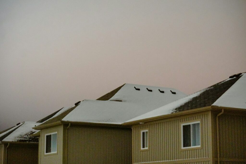 Snow-covered pitched roof beside a low-slope roof with visible gutters, flashing, and winter drainage details.