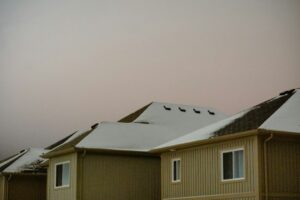 Snow-covered pitched roof beside a low-slope roof with visible gutters, flashing, and winter drainage details.